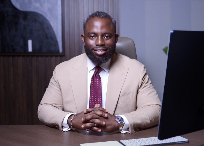 Headshot: beige suit, seated at a desk