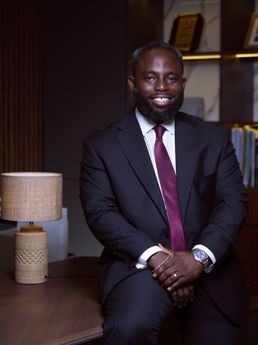 Headshot: dark suit, seated in an office