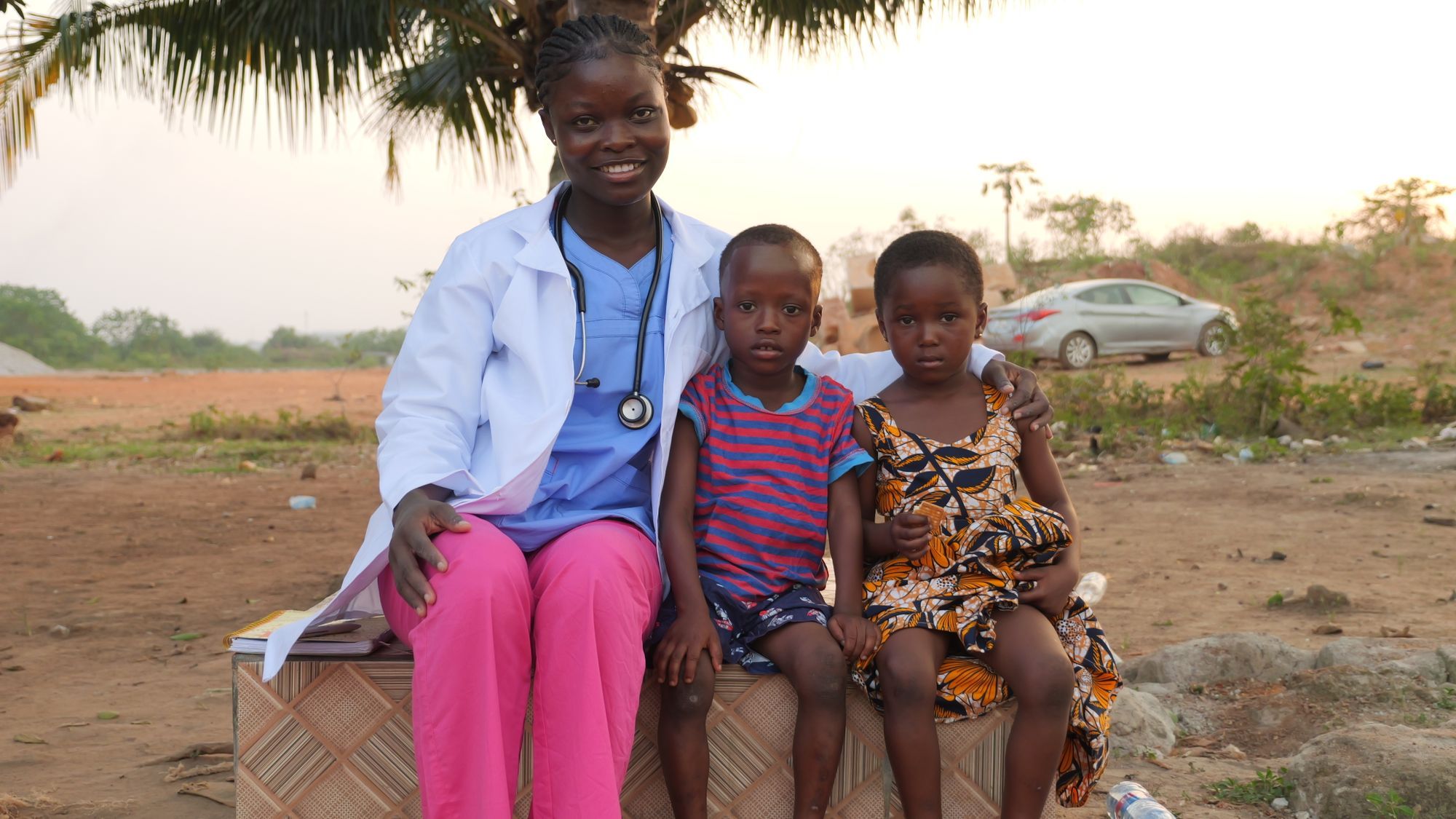 A smiling female health worker with two children outdoors
